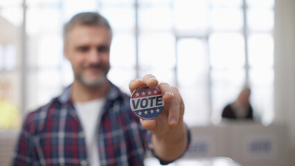 A smiling middle-aged man holding out a vote button on camera, asserting his voting right and duty