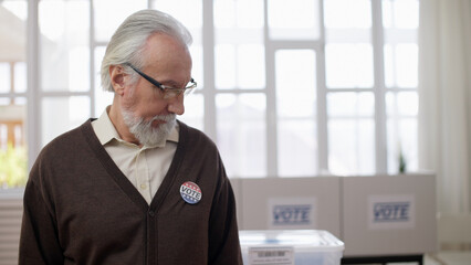 A senior man in eyeglasses looking at the vote pin attached to his chest during the US elections