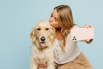 Young owner woman with her best friend retriever wears casual clothes do selfie shot on mobile cell phone kiss dog isolated on plain pastel light blue background studio. Take care about pet concept.