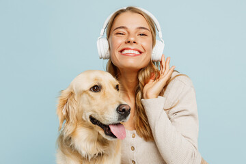 Young owner woman with her best friend retriever wear casual clothes listen to music in headphones hug cuddle embrace dog isolated on plain pastel light blue background. Take care about pet concept.