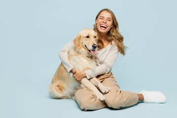 Full body overjoyed happy young owner woman wearing casual clothes sitting hug cuddle embrace her best friend retriever dog isolated on plain light blue background studio. Take care about pet concept.