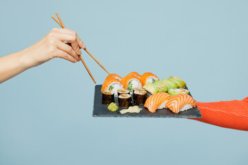 Close up cropped female hold in hand arm raw fresh sushi roll served on black plate isolated on...