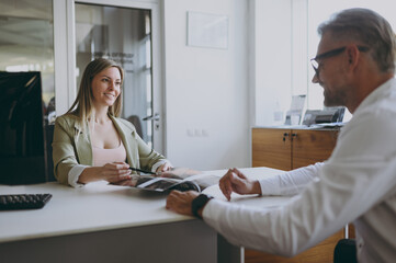 Adult man customer male buyer client wears shirt read catalog consult with salesman sit at table...