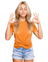 Fototapeta na wymiar Young blonde girl wearing casual clothes relax and smiling with eyes closed doing meditation gesture with fingers. yoga concept.