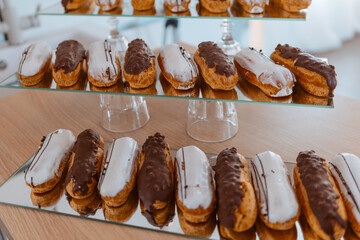 Eclairs with white and chocolate icing are laid out in a row on a mirror surface, display in a store.