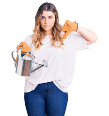 Young caucasian woman wearing gloves holding watering can with angry face, negative sign showing...