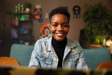 Portrait of delighted afro american woman in casual denim outfit smiling at camera sitting in...