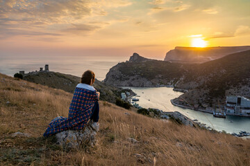 Happy woman on sunset in mountains. Woman siting with her back on the sunset in nature in summer....