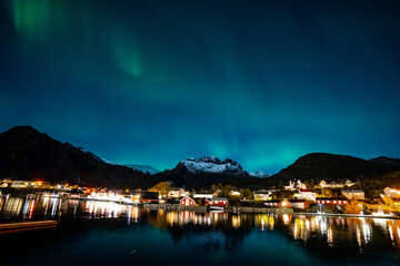 bright aurora borealis over a small coastal Sørvågen village on lofoten islands in norway with...