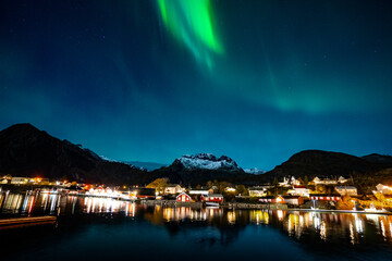 bright aurora borealis over a small coastal Sørvågen village on lofoten islands in norway with...