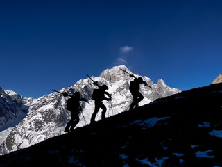 Silhouette of three backcountry skiers climbing up a mountain ridge with Mount Blanc as a backdrop.