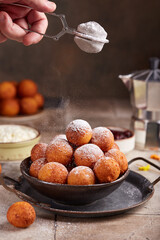 Deep fried cottage cheese balls or donuts. Freshly baked sweet croquettes, served sugar powder. Delicious homemade dessert. Man hand covering donuts with sugar powder.
