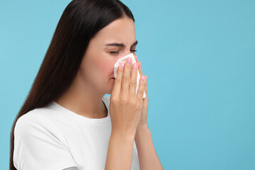 Suffering from allergy. Young woman blowing her nose in tissue on light blue background. Space for text