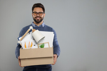 Happy unemployed man with box of personal office belongings on light grey background. Space for text