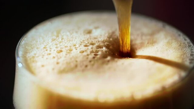 Beer pouring into the glass, close-up of dark beer foam.