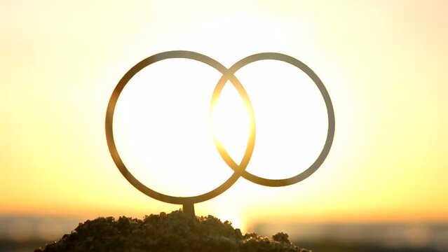 Black outlines of wedding rings at dawn and sunset on yellow sky. Stick contours in shape of wedding rings in sand on backdrop of setting and rising sun. Concept wedding love romantic Valentine's Day