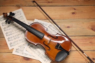 Violin, bow and music sheets on wooden table, top view