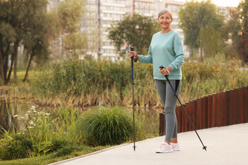 Senior woman performing Nordic walking outdoors, space for text