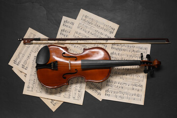 Violin, bow and music sheets on black table, top view