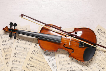 Violin, bow and music sheets on white wooden table, top view