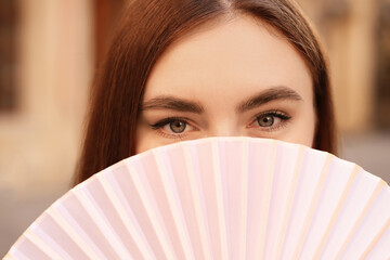 Young woman holding hand fan outdoors, closeup