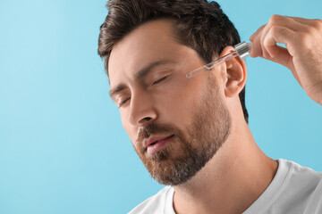 Obraz premium Handsome man applying cosmetic serum onto his face on light blue background, closeup. Space for text