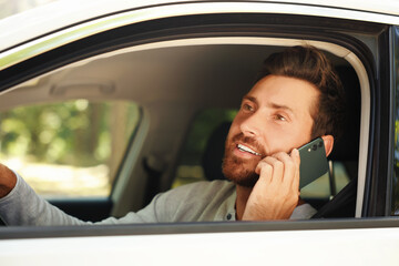 Happy bearded man talking on smartphone in car, view from outside