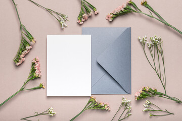 Gray envelope and blank form with flowers on a brown background. Greeting card, mockup.