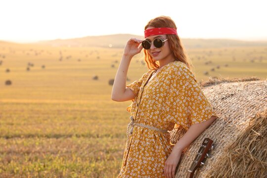 Happy hippie woman near hay bale in field, space for text