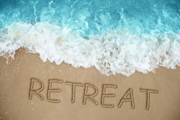 Word Retreat drawn on sand near sea, above view