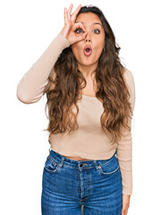 Fototapeta premium Young hispanic girl wearing casual clothes doing ok gesture shocked with surprised face, eye looking through fingers. unbelieving expression.
