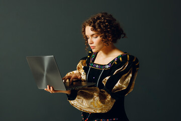 Portrait of a young aristocratic woman dressed in a medieval dress working on laptop