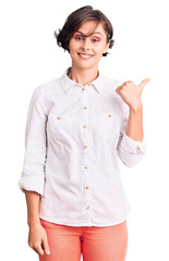 Beautiful young woman with short hair wearing elegant white shirt smiling with happy face looking and pointing to the side with thumb up.