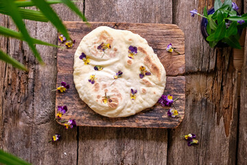 flatbread with edible flowers. Viola, top view, wooden background