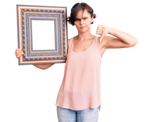 Beautiful young woman with short hair holding empty frame with angry face, negative sign showing dislike with thumbs down, rejection concept
