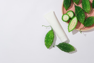 Against a white background, fresh bitter melons and bitter melon slices decorated with white bottle mockup for cosmetic. Top view, empty space for text and design. Scene for advertising