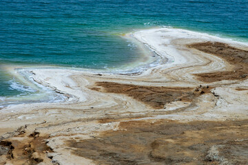 Jordan. Shore of Dead Sea with traces of shallowing. White salt deposits - rocks covered with crystals - are located along the entire coastline, separating turquoise waters of Dead Sea from shore.
