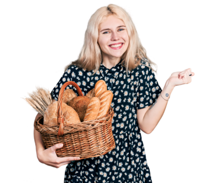Young caucasian woman holding wicker basket with bread screaming proud, celebrating victory and success very excited with raised arm