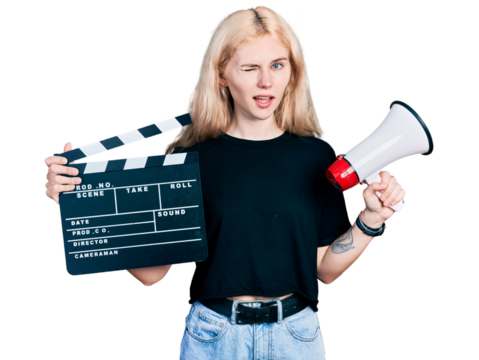 Young caucasian woman holding video film clapboard and megaphone winking looking at the camera with sexy expression, cheerful and happy face.