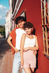 Young smiling beautiful woman and her handsome boyfriend in casual summer clothes. Happy cheerful family. Female having fun. Couple posing in street at sunny day. Near red wall at sunset