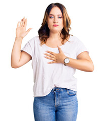 Young beautiful caucasian woman wearing casual white tshirt swearing with hand on chest and open...