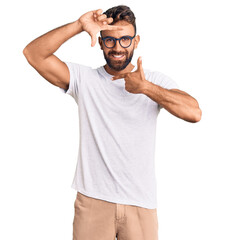 Young hispanic man wearing casual clothes and glasses smiling making frame with hands and fingers with happy face. creativity and photography concept.