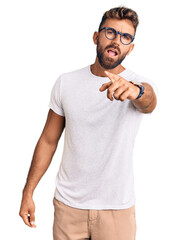 Young hispanic man wearing casual clothes and glasses pointing displeased and frustrated to the...