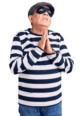 Naklejka premium Senior handsome man wearing burglar mask and t-shirt begging and praying with hands together with hope expression on face very emotional and worried. begging.