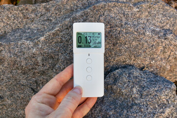 Dosimeter radiometer in hand measuring the level of ionizing radiation from granite stone