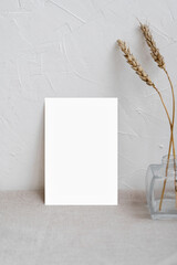 Minimalist home interior poster or picture frame design template, blank paper card mockup on neutral beige table, vase with dried meadow grass, empty white plaster textured wall background