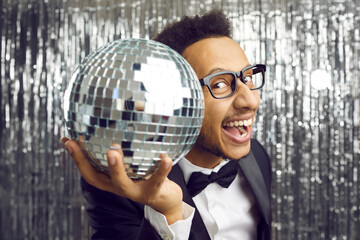 Happy young African American man showing disco ball with smile inviting to nightclub for party or...