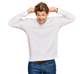 Handsome caucasian man wearing casual white sweater smiling pulling ears with fingers, funny...