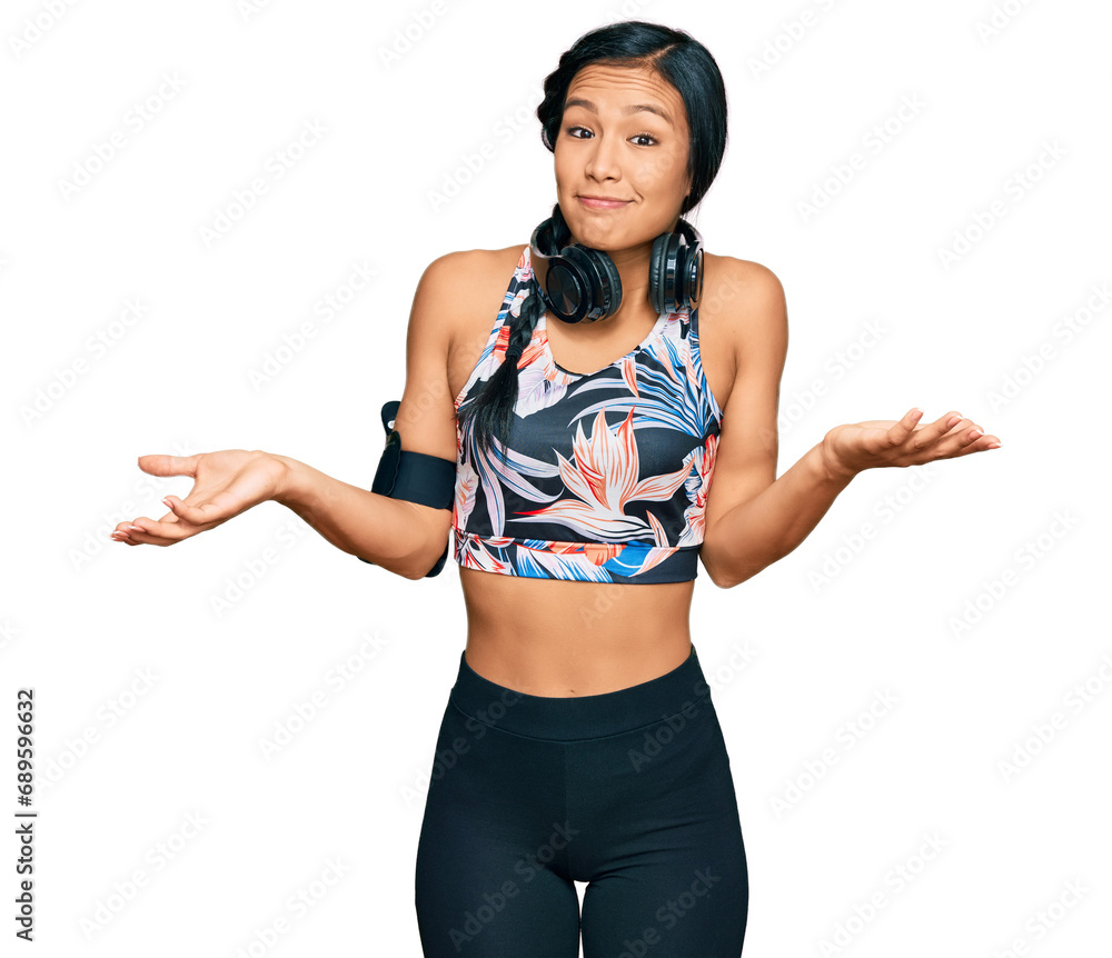 Sticker beautiful hispanic woman wearing sportswear and headphones clueless and confused expression with arm