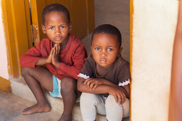 village african kids boy and girl sited together in front of the house, waiting for mom to come...